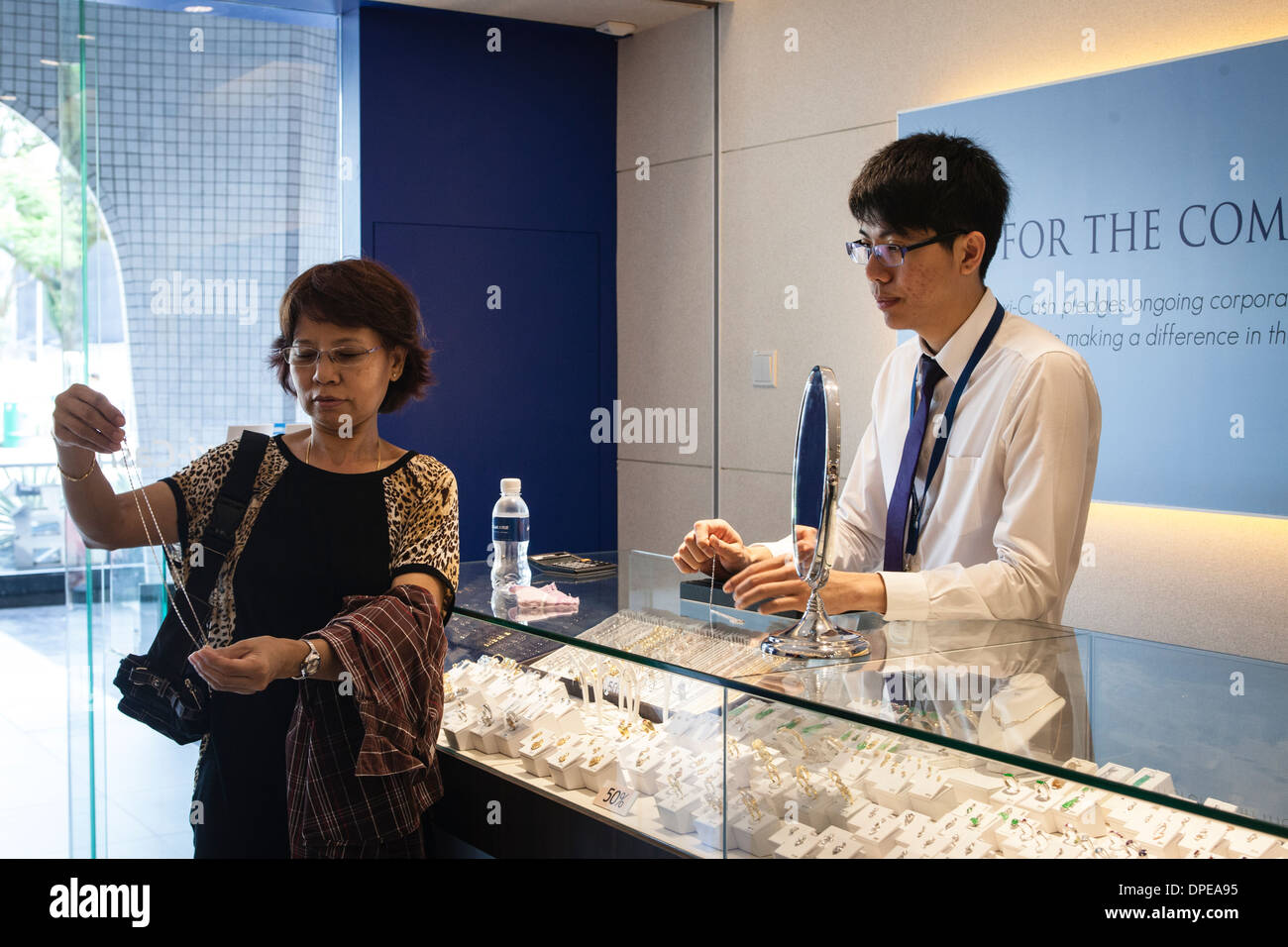 A salesperson looks on as a customer examines a gold chain at a branch