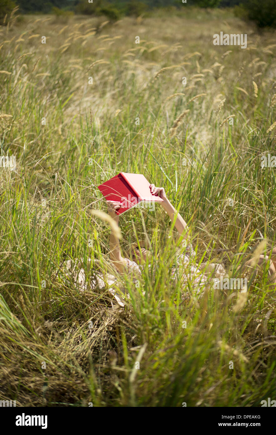 Woman lying in long grass reading book Stock Photo