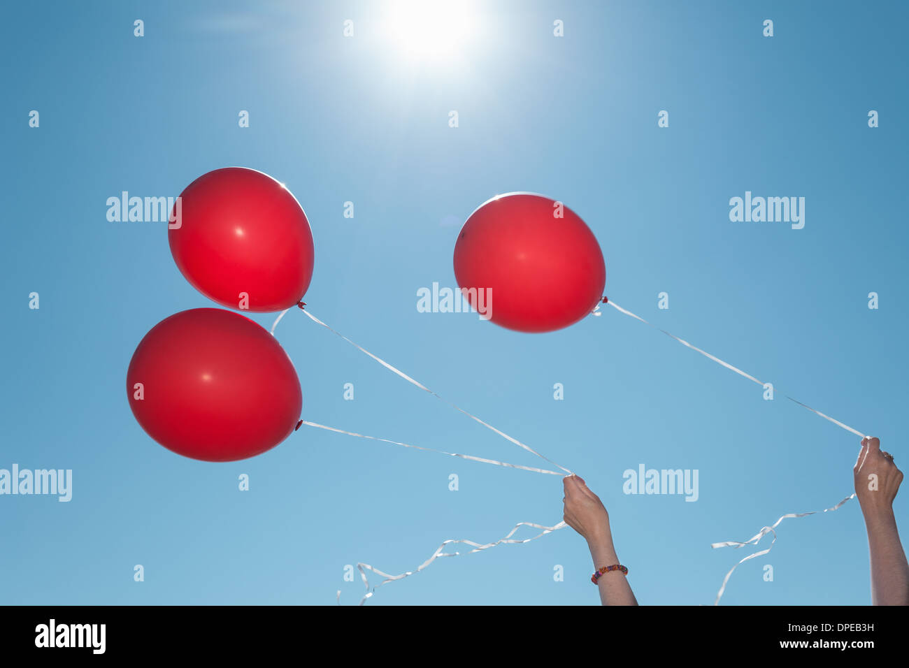 Hands holding three red balloons against blue sky Stock Photo - Alamy