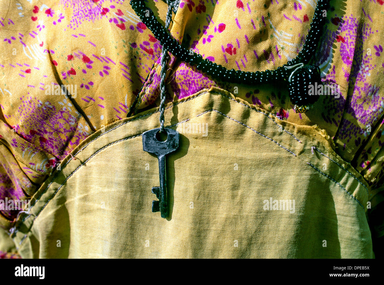 Detail of a yellow patterned hand-made dress & a key necklace worn by a young female lower caste construction worker in Delhi Stock Photo