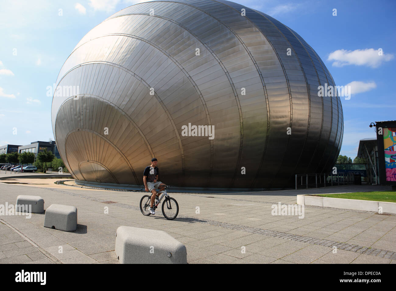 Cyclist passing the titanium clad building which forms part of the Glasgow Science Centre Stock Photo