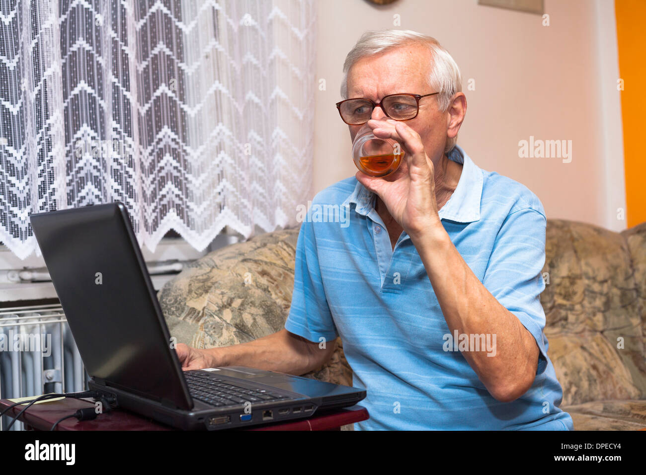 Senior man using laptop and drinking whiskey at home. Stock Photo