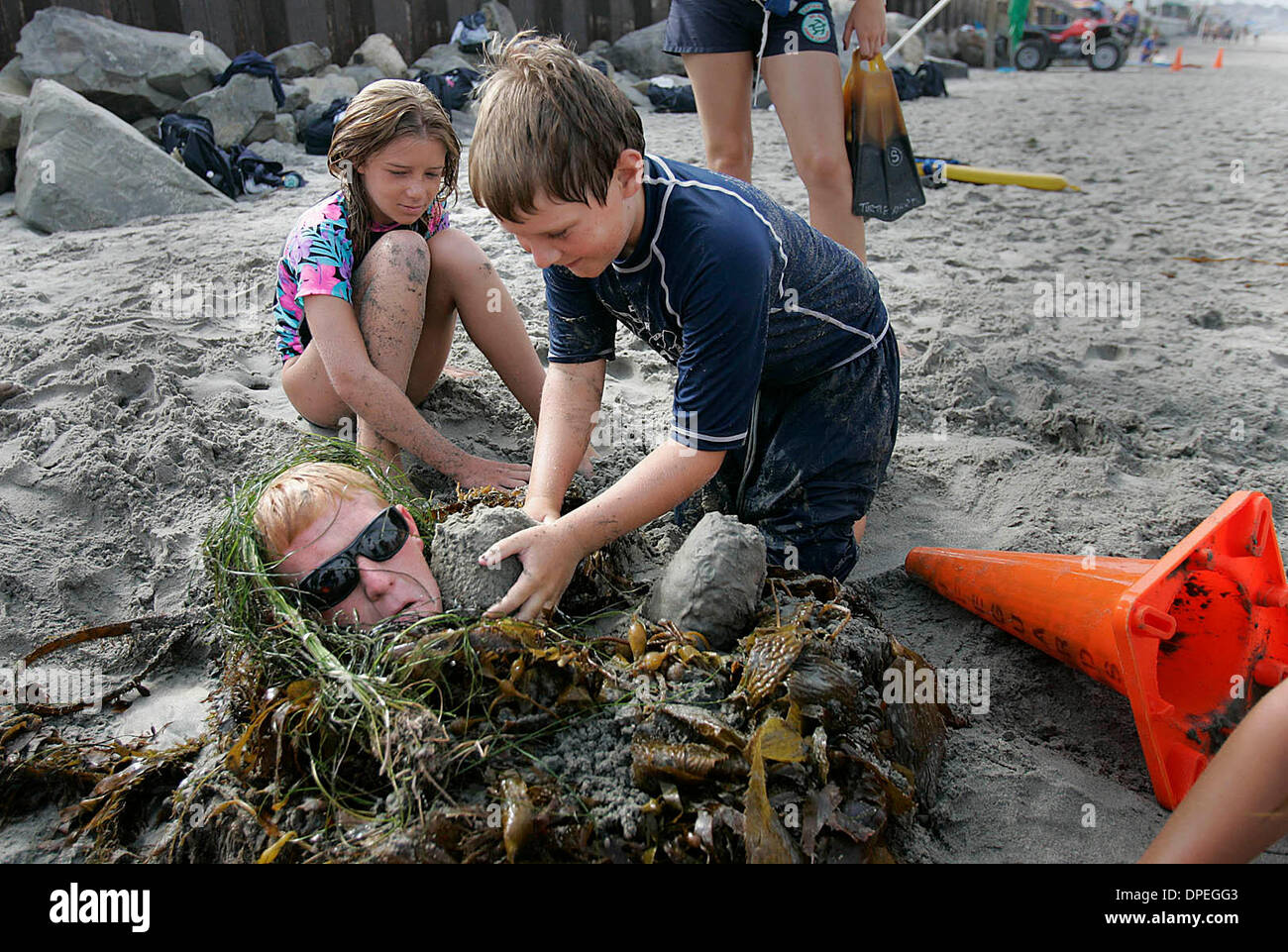 (Published 7/22/2006, NC-1, NI-1) JULY 20, 2006 Junior lifeguard BOBBY WRIGHT(cq), right, applies packed sand to the face of his mentor, lifeguard BRIAN REAGAN(cq)who was buried up to his neck in sand on the beach at 29th Street in Del Mar Thursday.  At left is SKYLAR WIGGINS(cq).  Both junior guards are 11.  Lifeguards worked out with junior lifeguards on the beach at Del Mar on t Stock Photo