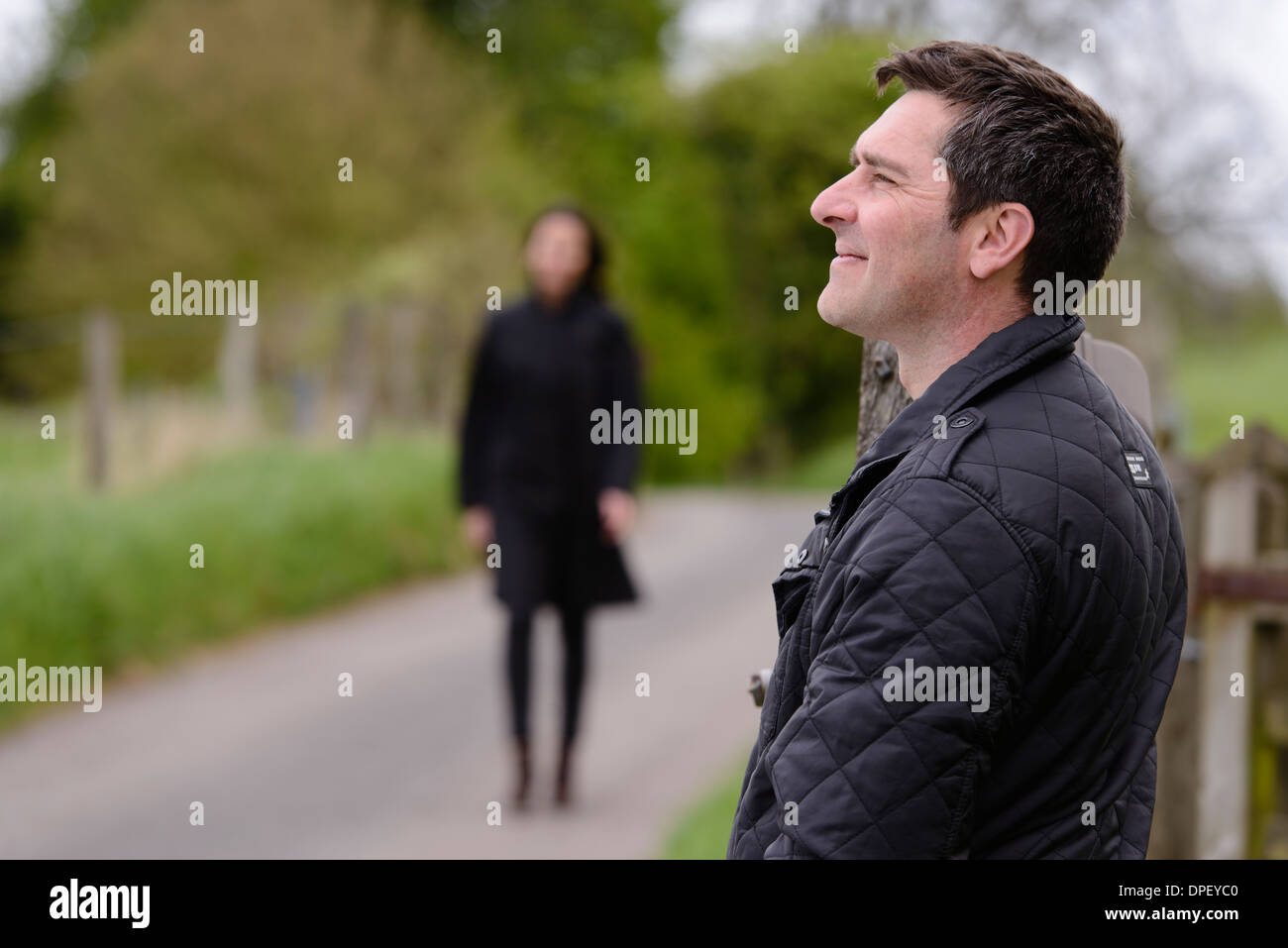A man waiting by the side of the road is approached by a woman. Stock Photo