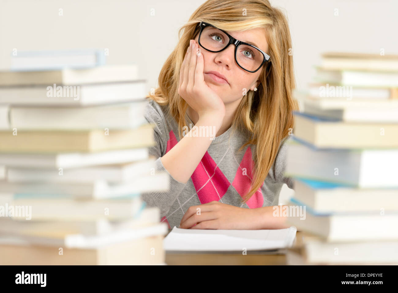 Bored student girl between stack of books looking up glasses Stock Photo