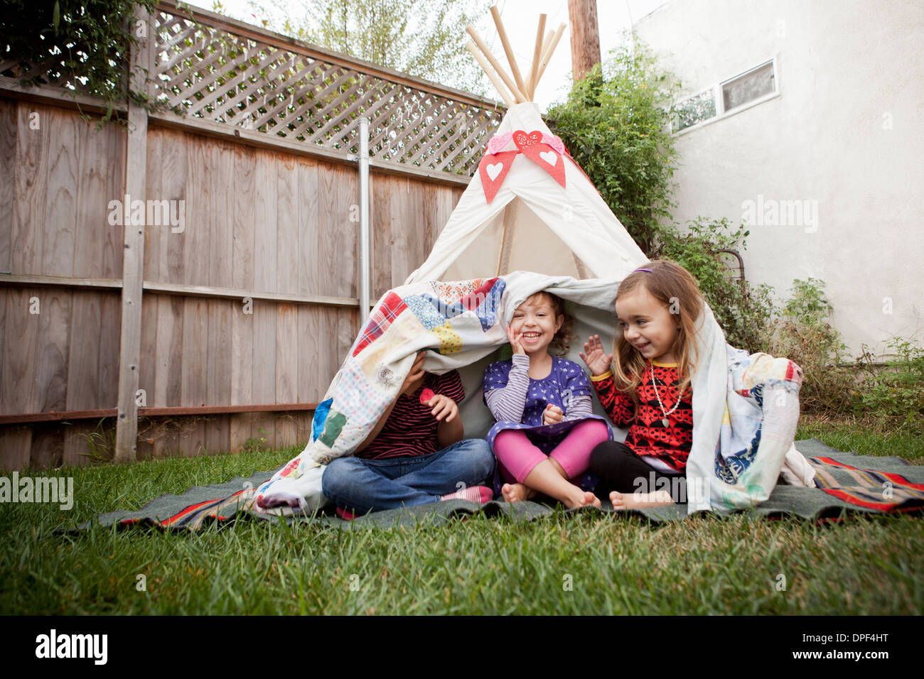 Three young girls in garden hiding under blanket Stock Photo