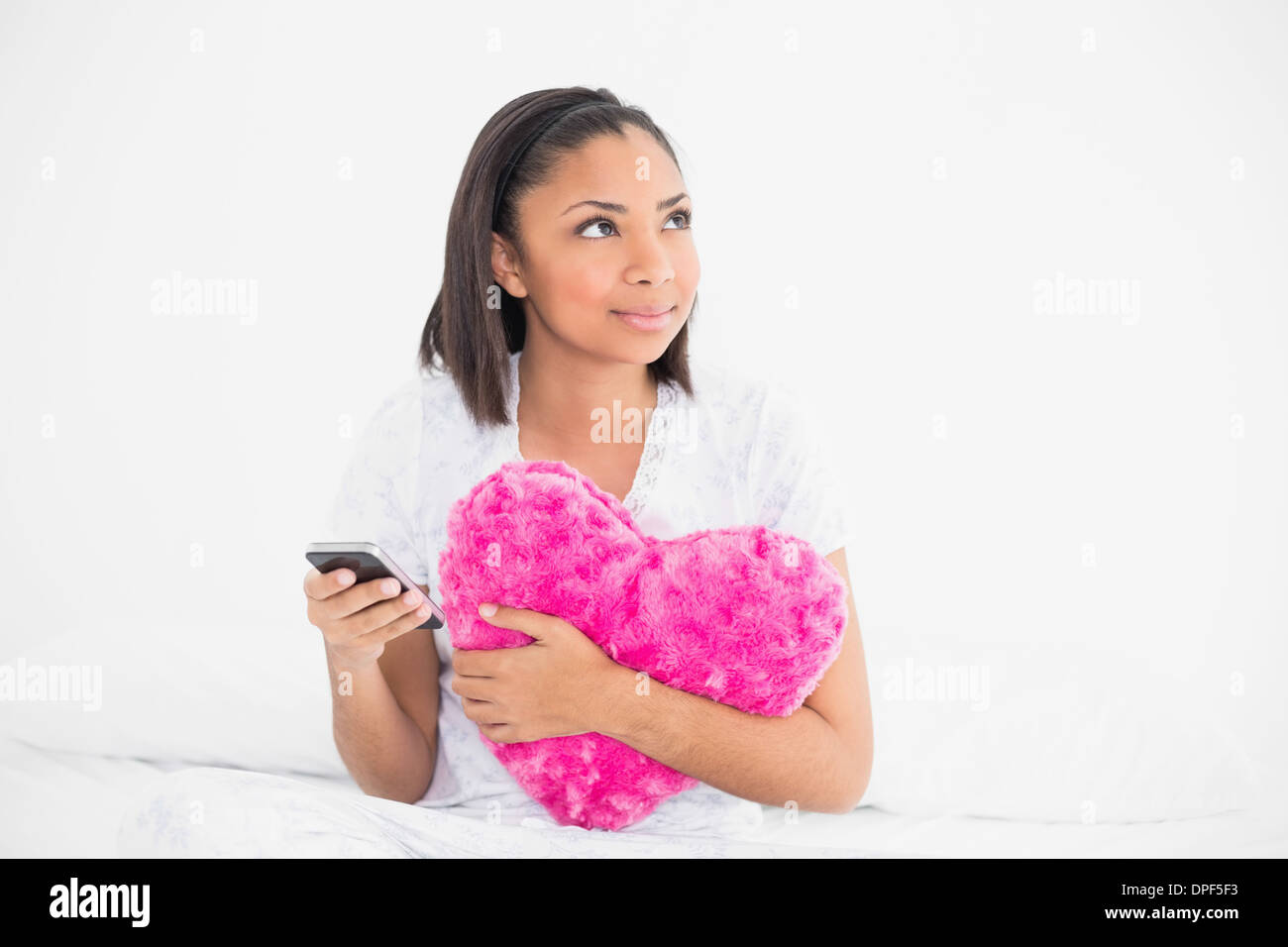 Thoughtful young dark haired model holding a pillow and a mobile phone Stock Photo
