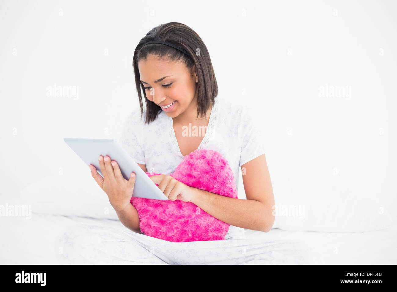 Concentrated young dark haired model holding a pillow and using a tablet pc Stock Photo