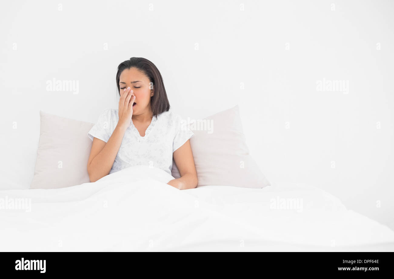 Exhausted young dark haired model yawning lying in her bed Stock Photo