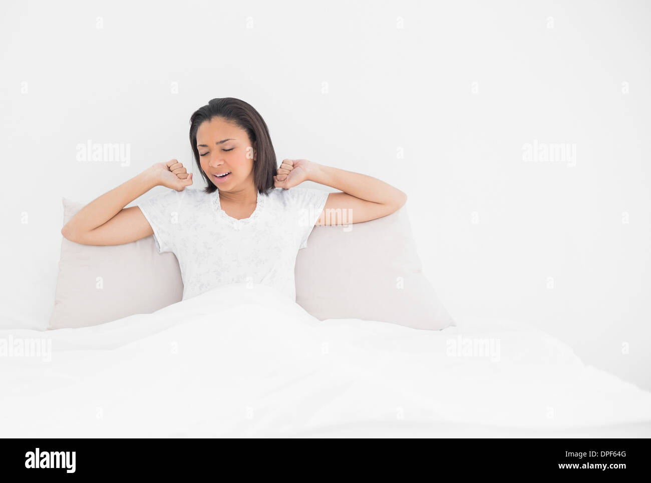 Tired young dark haired model stretching in her bed Stock Photo