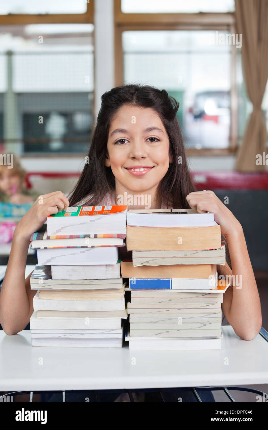Schoolgirl Smiling With Stacked Books At Desk Stock Photo - Alamy