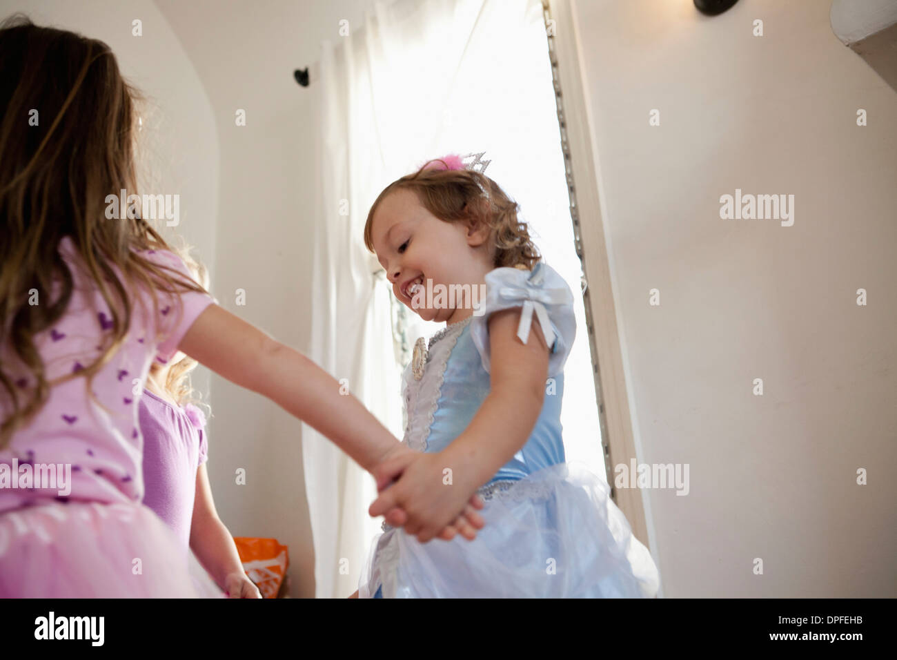 Three young girls in party dress dancing in circle Stock Photo