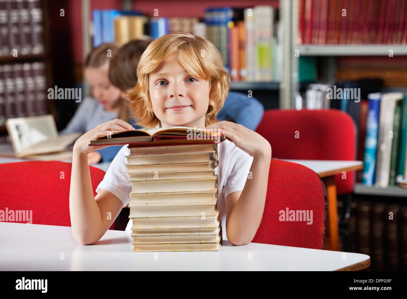 Schoolboy Sitting With Stack Of Books In Library Stock Photo - Alamy