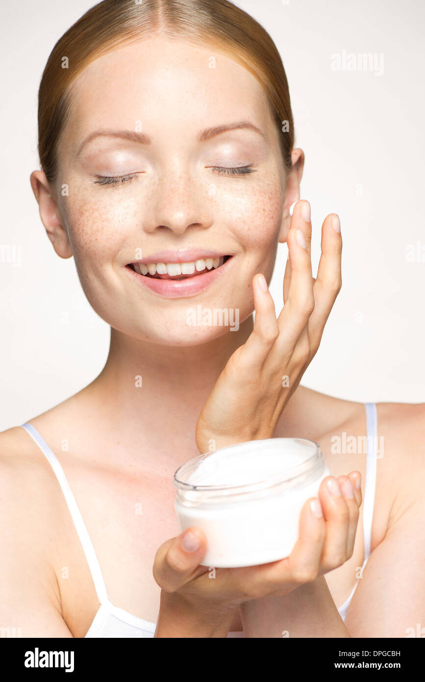 Youn woman moisturizing face with eyes closed Stock Photo