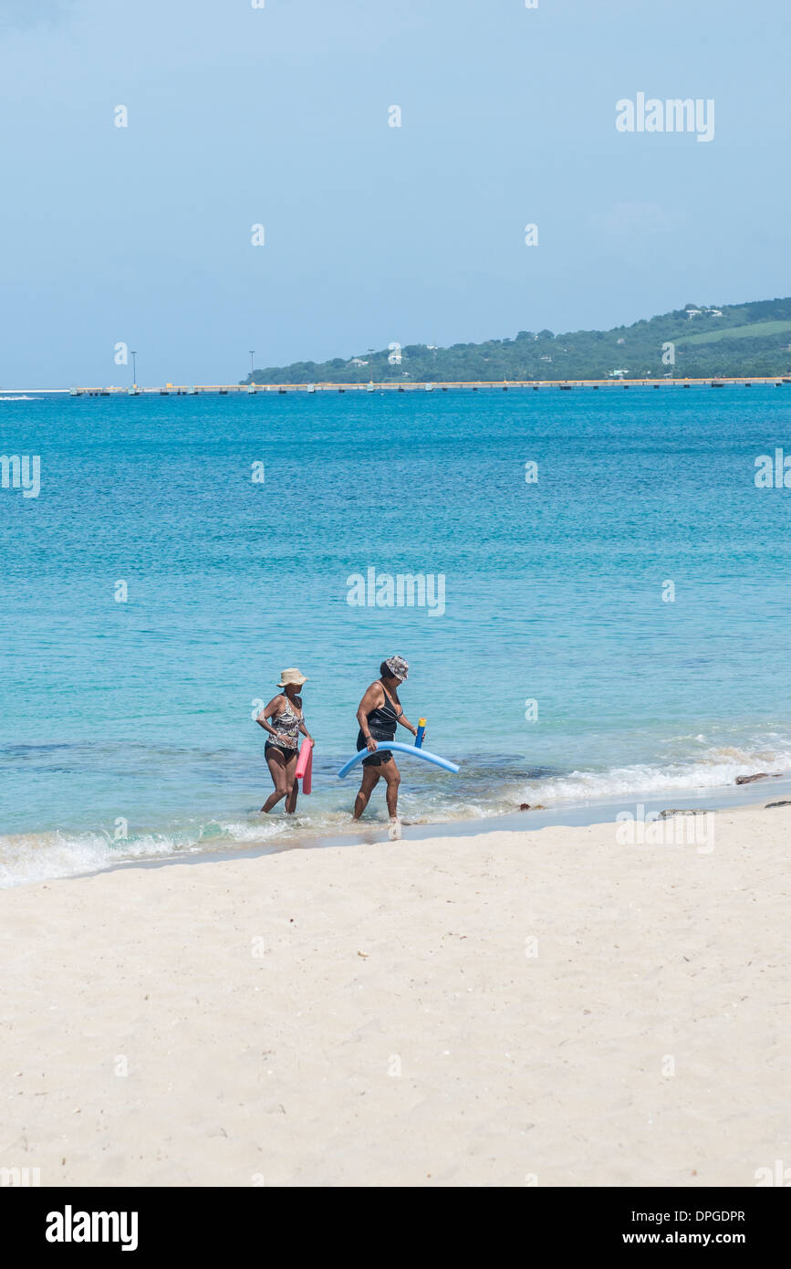 Two African American women, carrying floatation devices wade from the Caribbean sea onto the beach in St. Croix Stock Photo