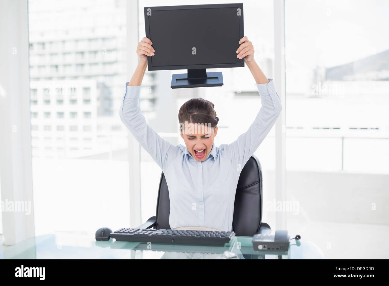 Angry classy brown haired businesswoman throwing her computer screen ...