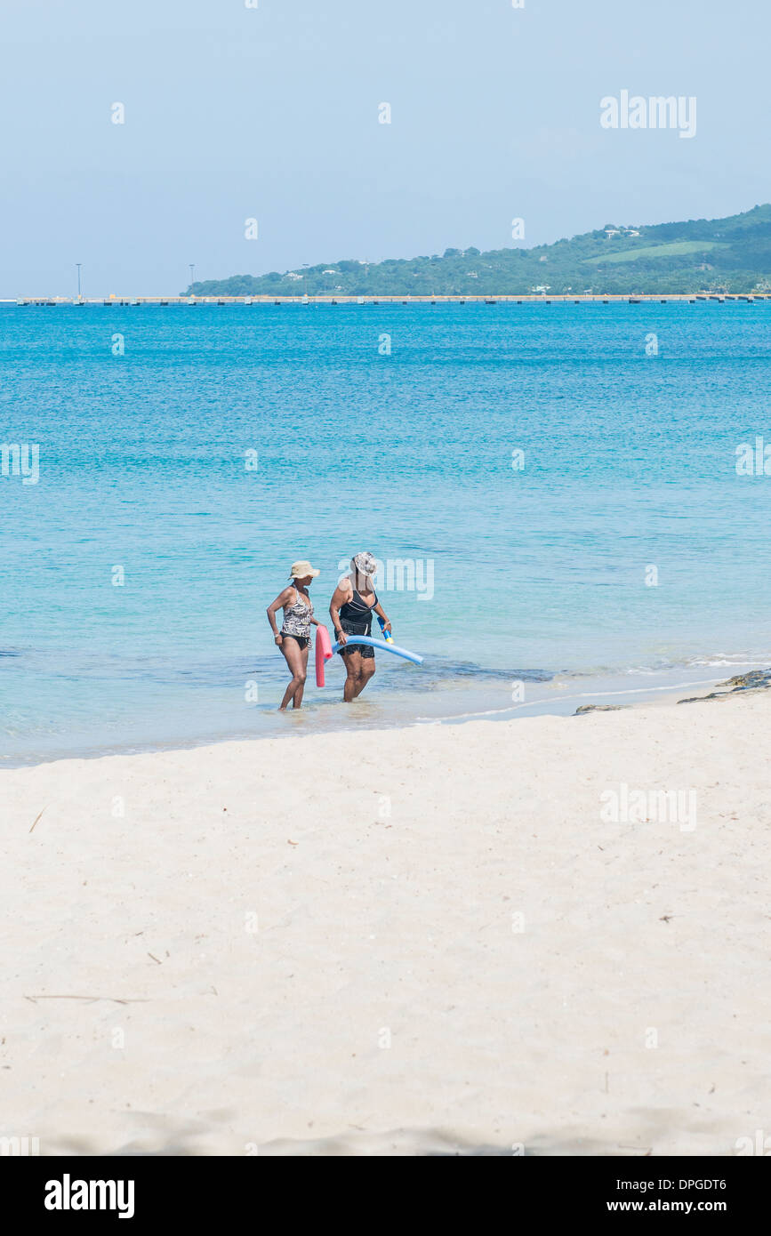 Two African American women, carrying floatation devices wade from the Caribbean sea onto Sandcastle Beach in St. Croix. Stock Photo