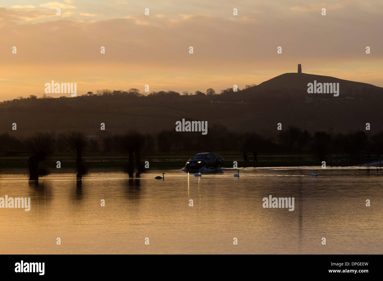 A jeep drives through a flooded road in front of Glastonbury Tor Stock Photo