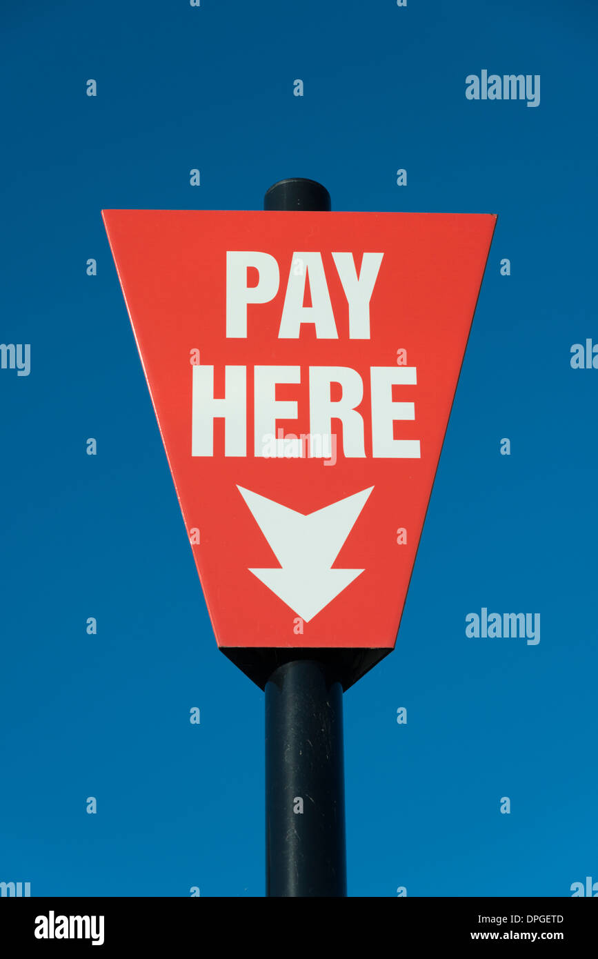 A pay here sign in a car park in the UK. Bright red colours against a blue sky Stock Photo
