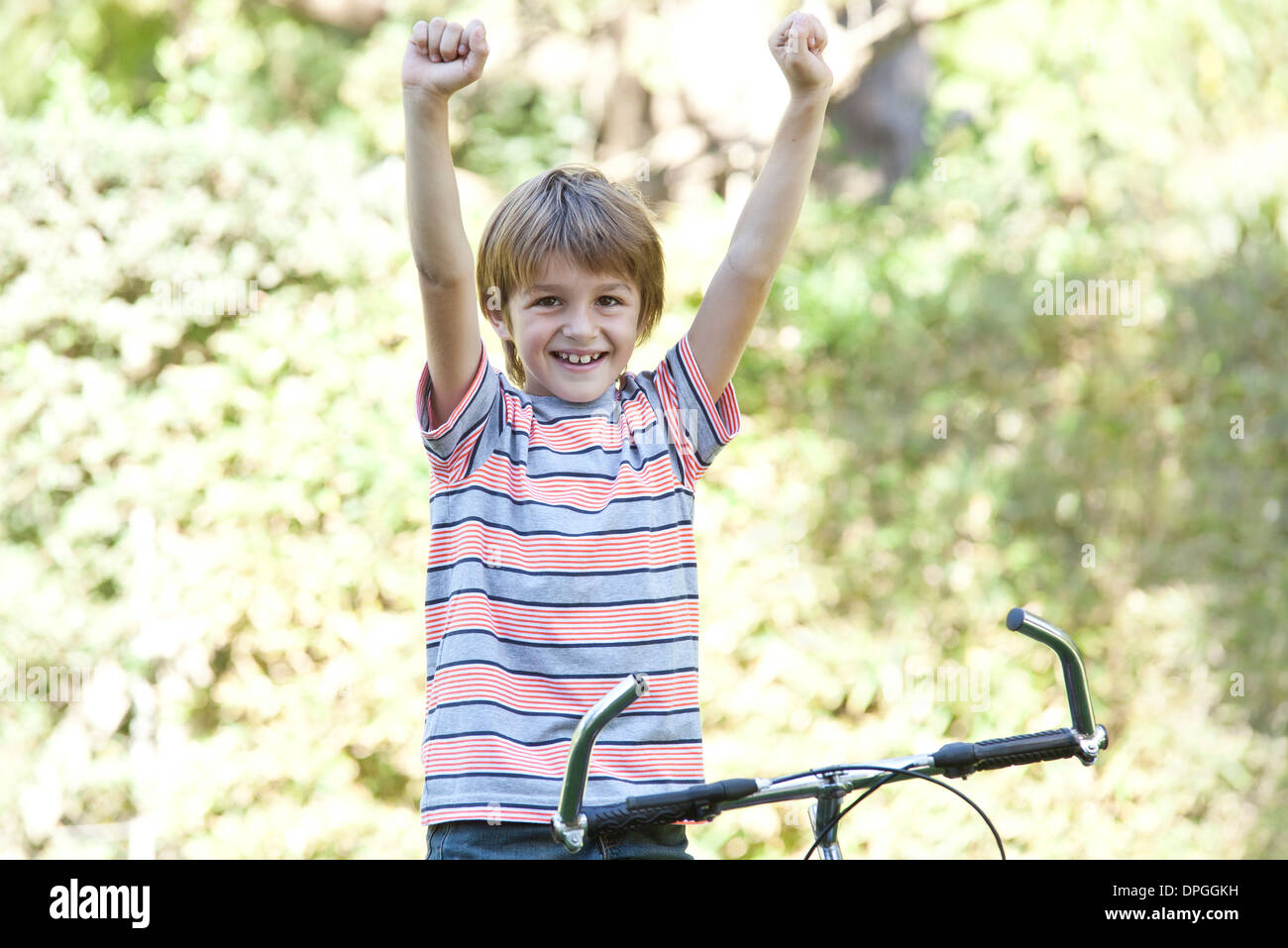 Boy riding bicycle, arms raised, portrait Stock Photo
