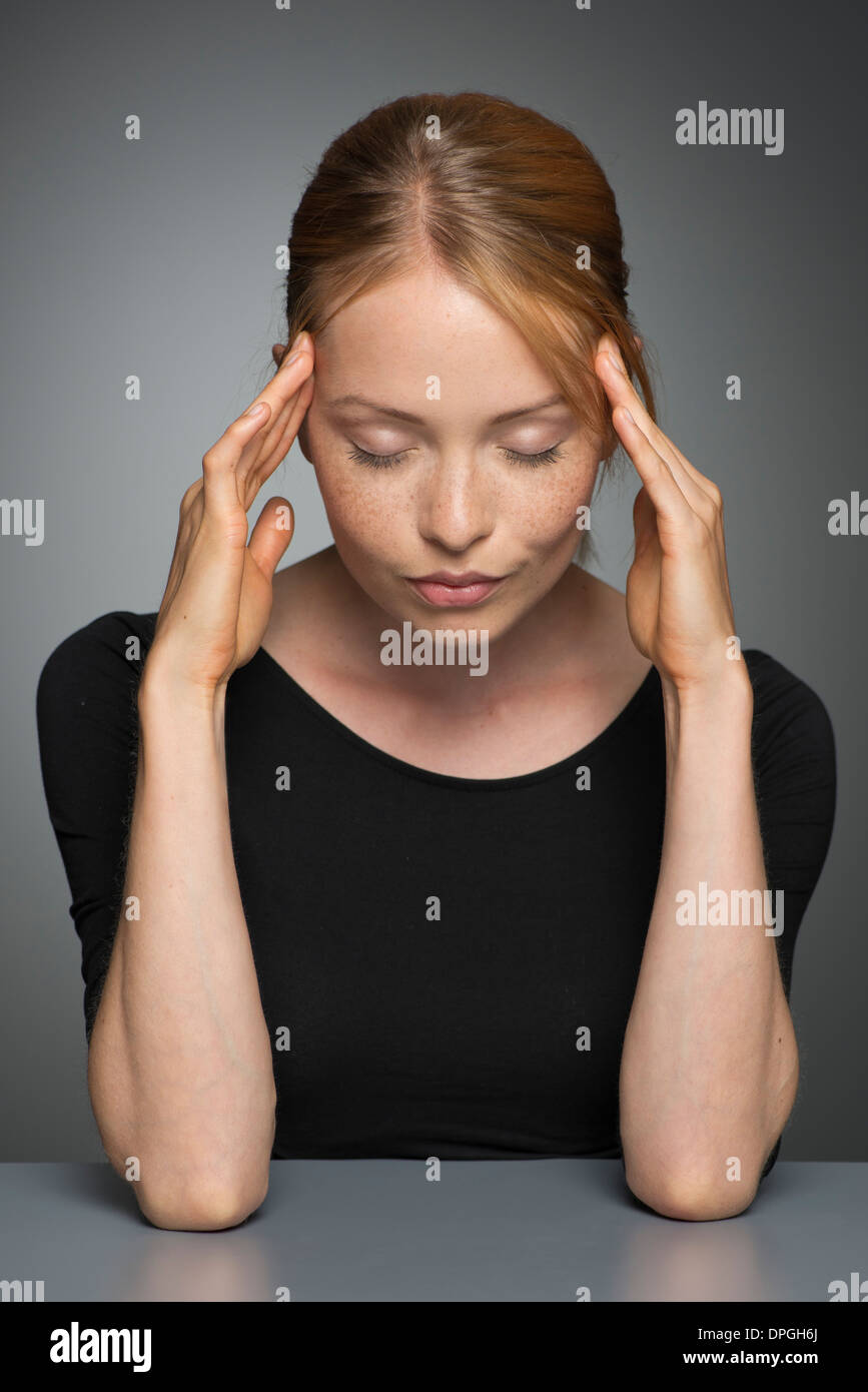 Young woman holding head, eyes closed Stock Photo