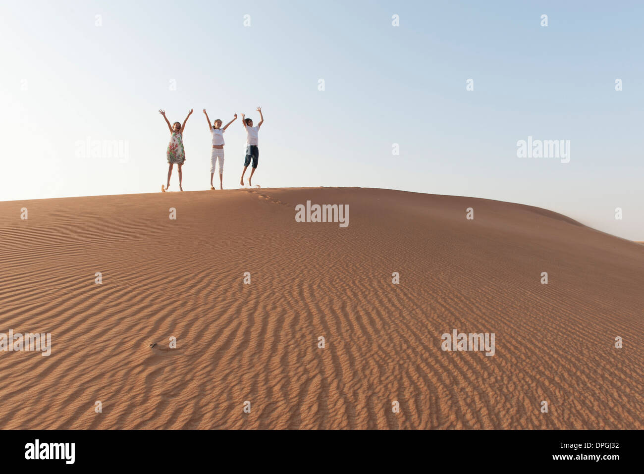 Children jumping on top of dune with arms raised in air Stock Photo