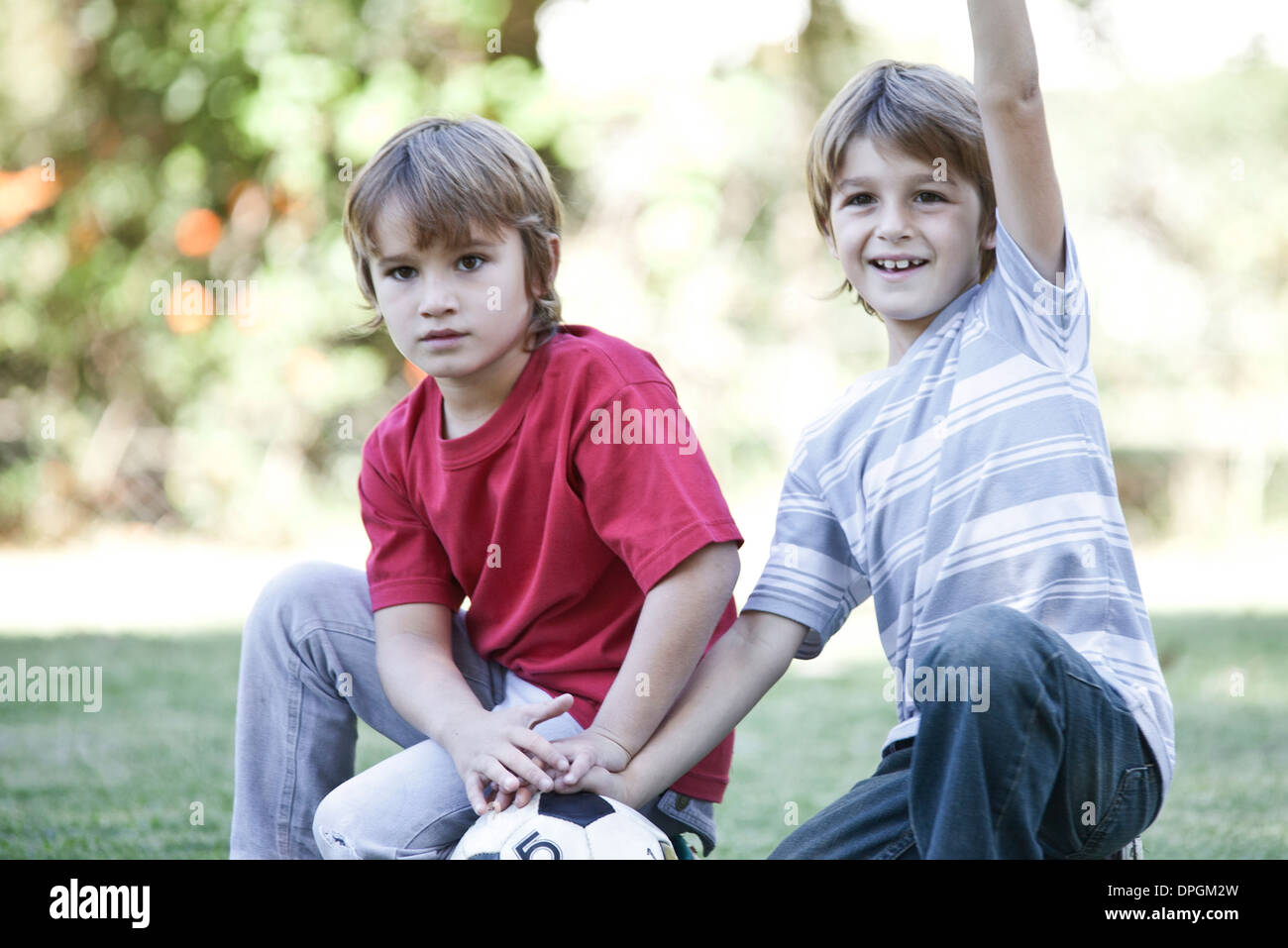Boys crouching on field with soccer ball, one boy cheering with arm in air Stock Photo