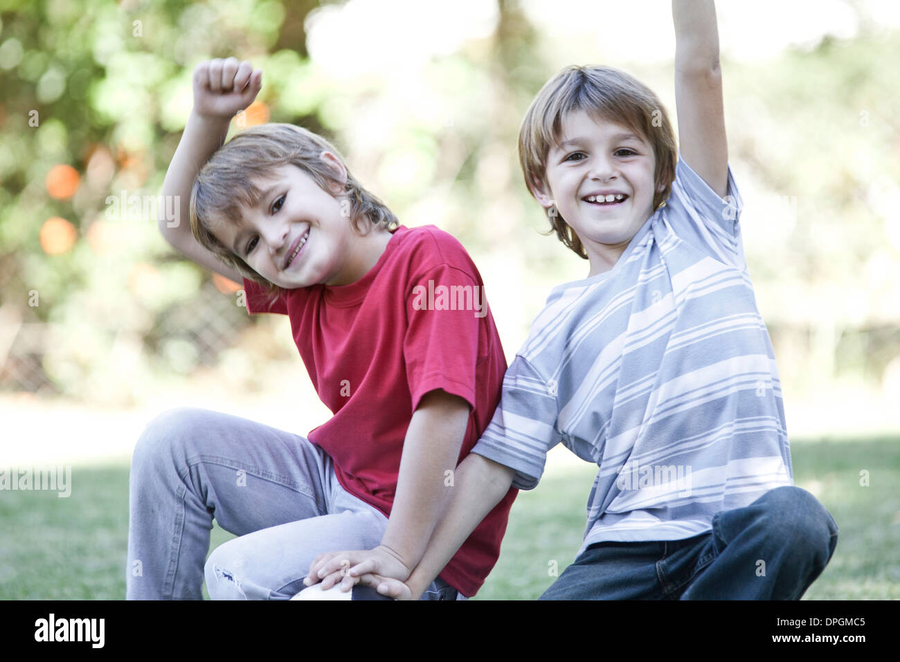 Boys crouching on field with soccer ball, both cheering with arms in air Stock Photo