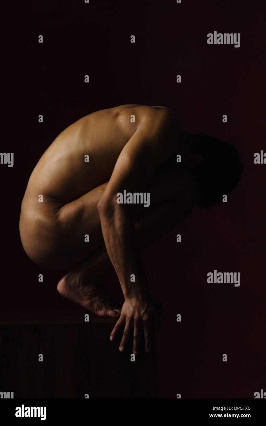 Nude man crouching in dark Stock Photo