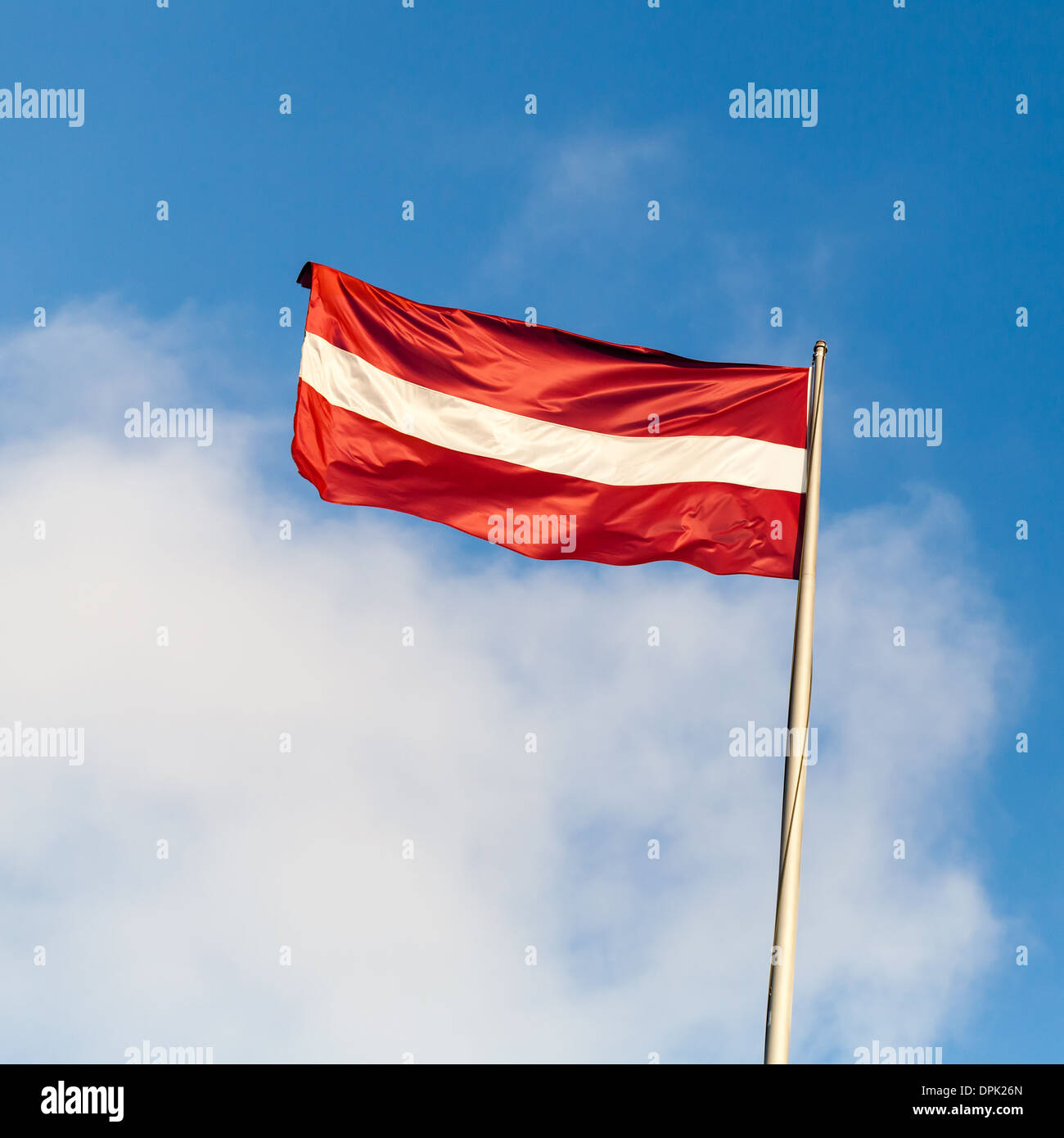 Flag of Latvia above blue sky with clouds Stock Photo