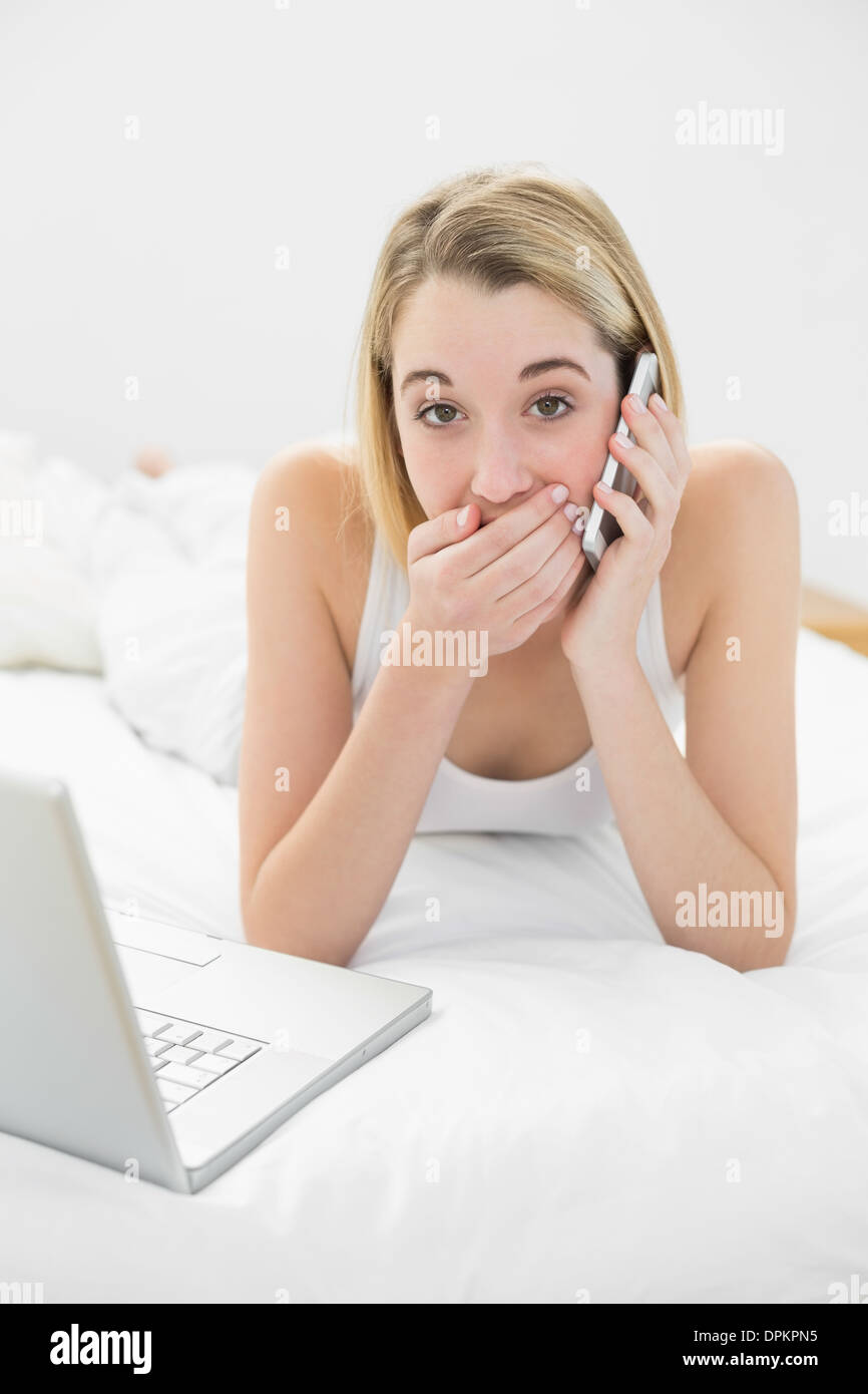 Portrait of attractive surprised woman phoning lying on her bed Stock Photo