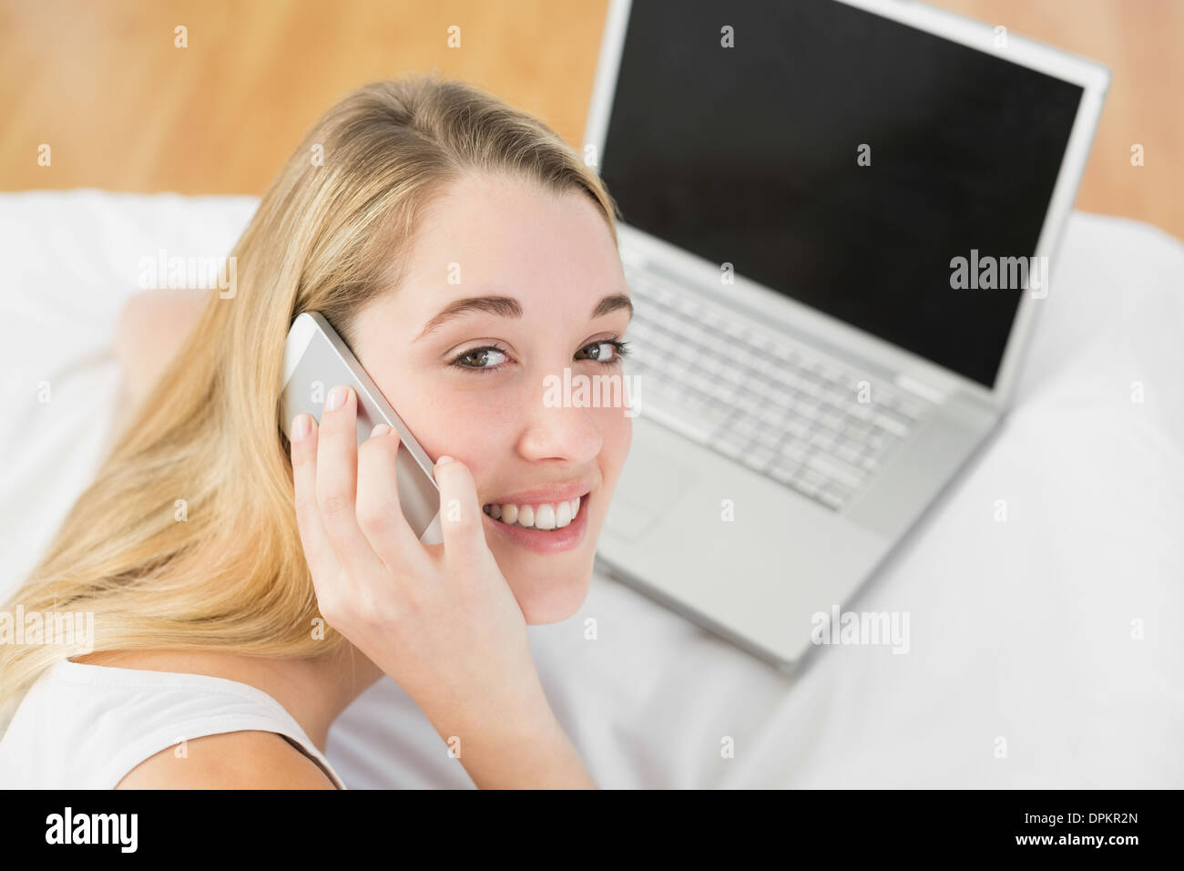 Beautiful woman phoning while lying on her bed next to her notebook Stock Photo