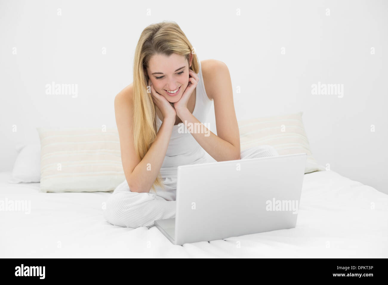 Gleeful young woman working with her laptop sitting on her bed Stock Photo