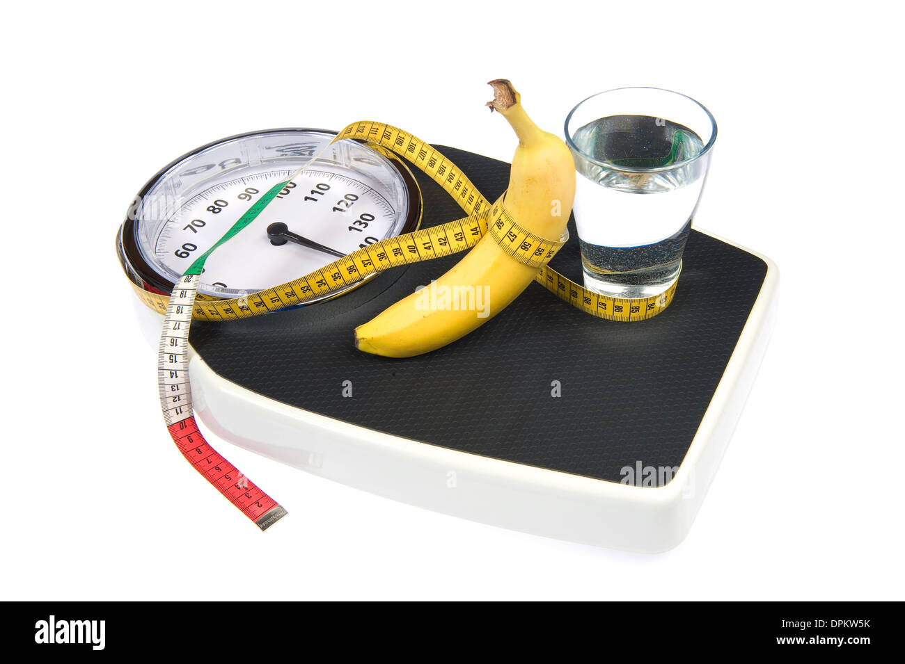 A weight scale with measuring tape, a banana and a glass of water Stock Photo
