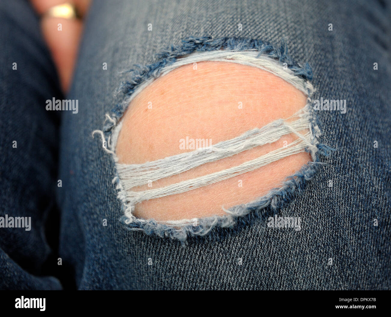 Denim jeans being worn with a large hole in the knee Stock Photo