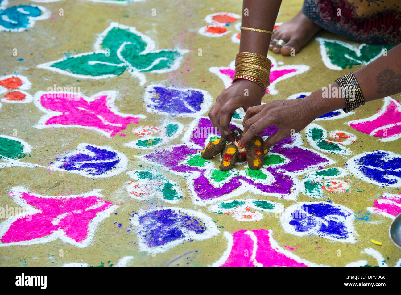 Indian womans hands making Rangoli festival coloured powder designs at