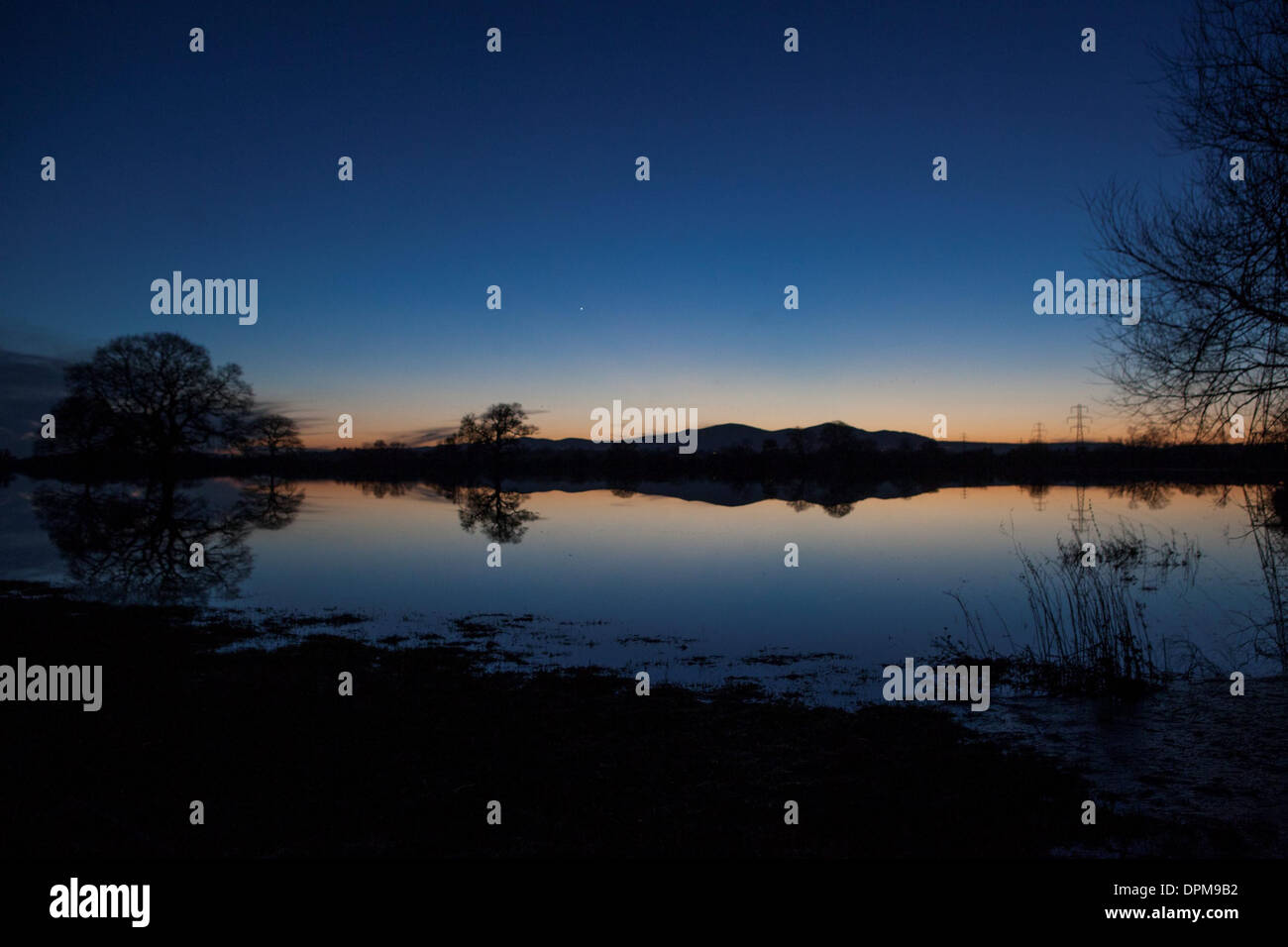 The sun sets behind the Malvern Hills in Worcester, reflected in flooded farmland Stock Photo