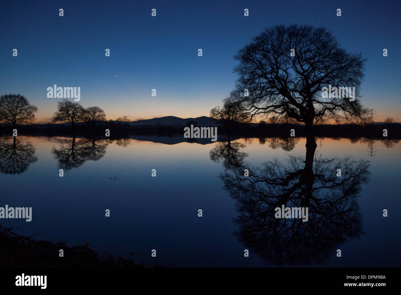 The sun sets behind the Malvern Hills in Worcester, reflected in flooded farmland Stock Photo