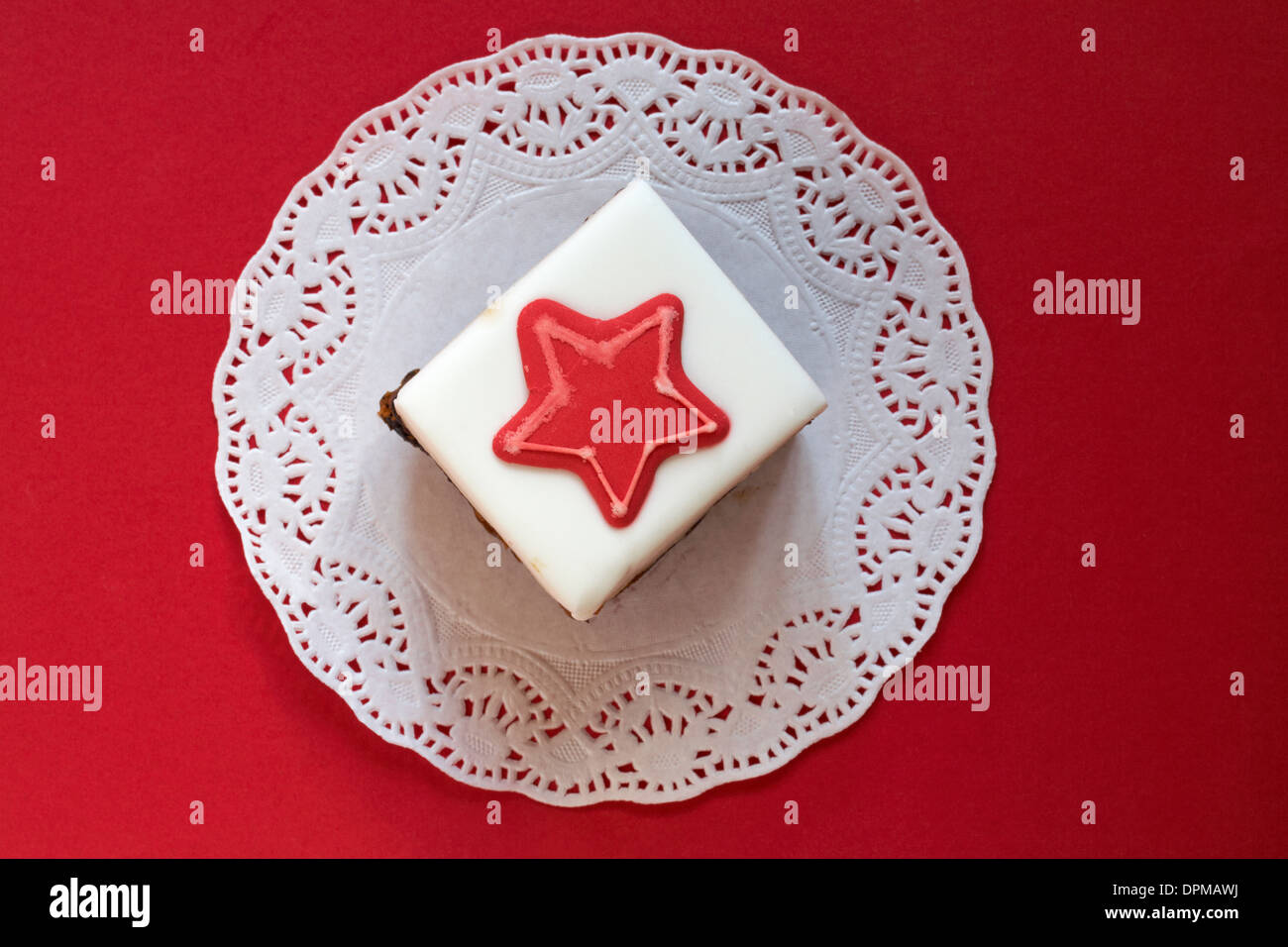 slab of Christmas cake with red star on icing set on doilee with red background Stock Photo