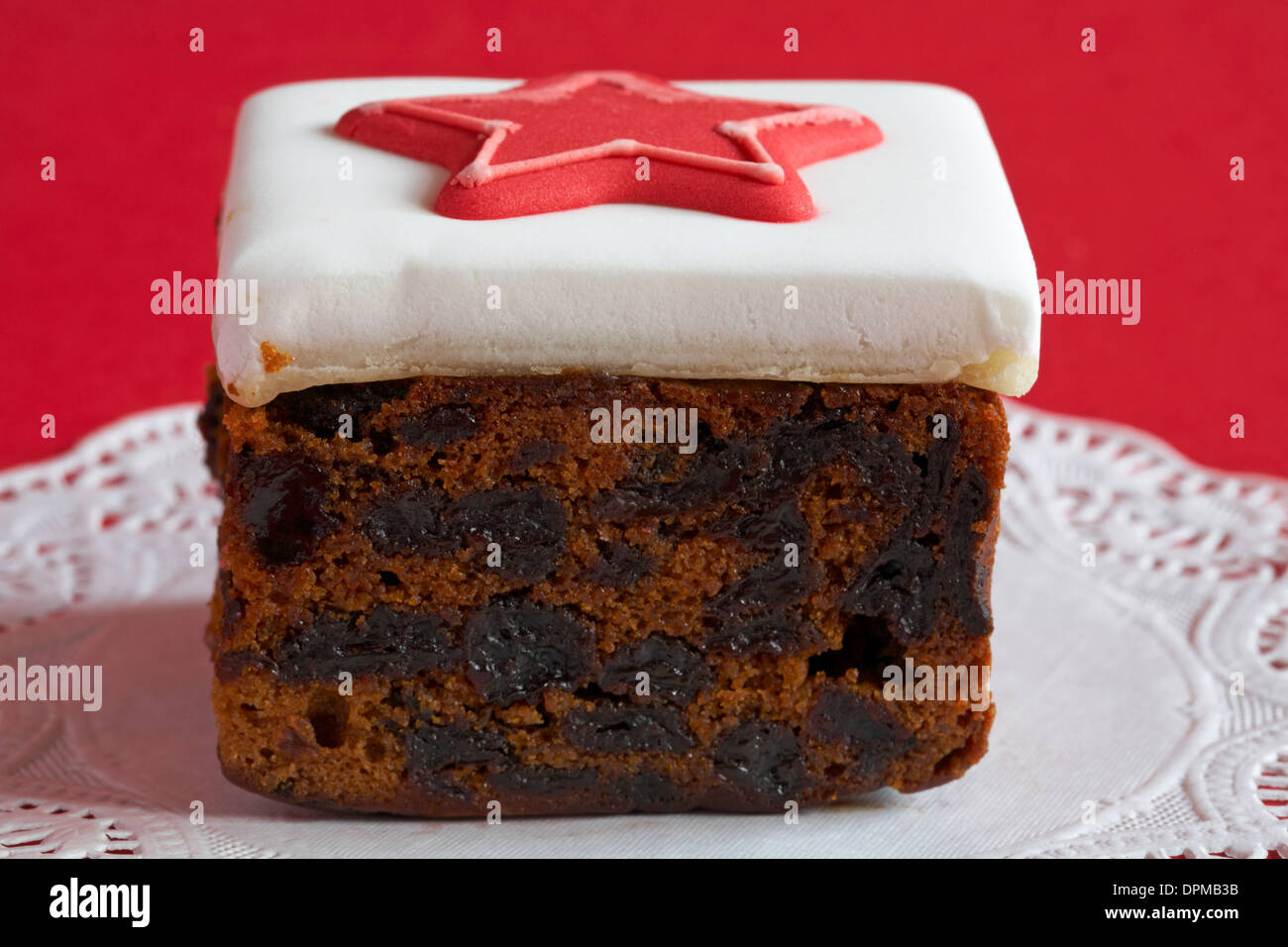 slab of Christmas cake with red star on icing set on doilee with red background Stock Photo