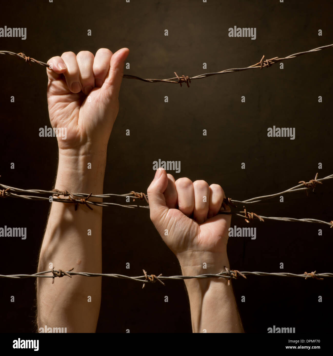 hands behind barbed wire with dark background Stock Photo