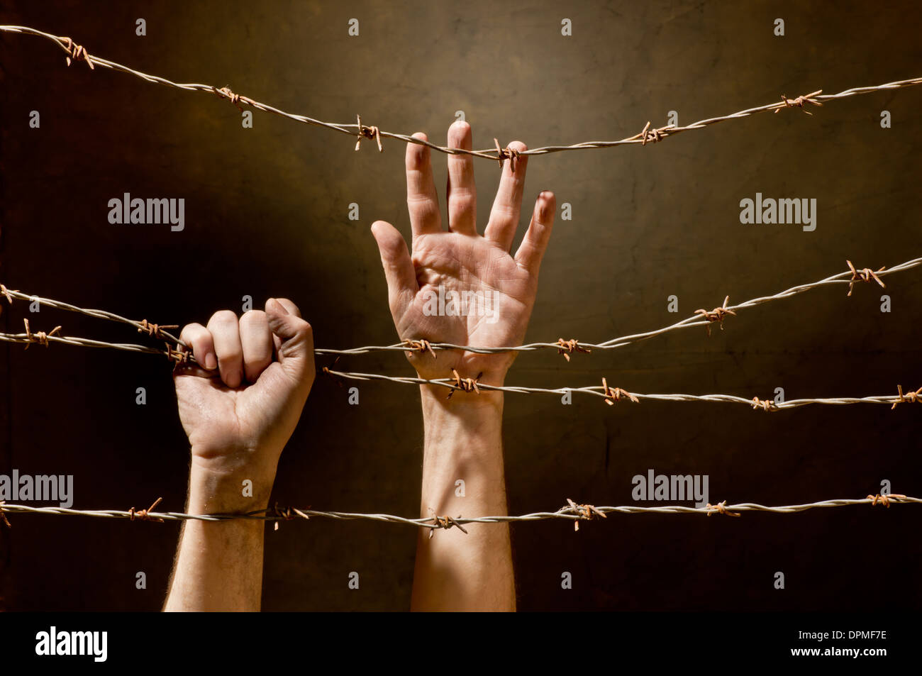 hands behind barbed wire with dark background Stock Photo