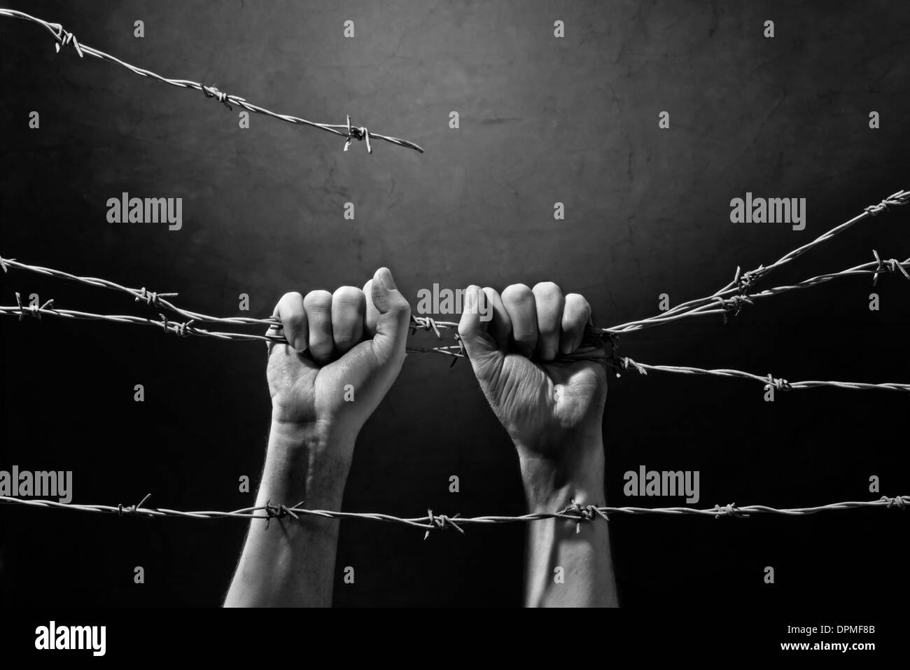 hands behind barbed wire with dark background Stock Photo