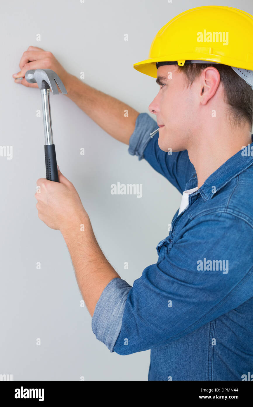 Side view of handyman hammering nail in wall Stock Photo Alamy