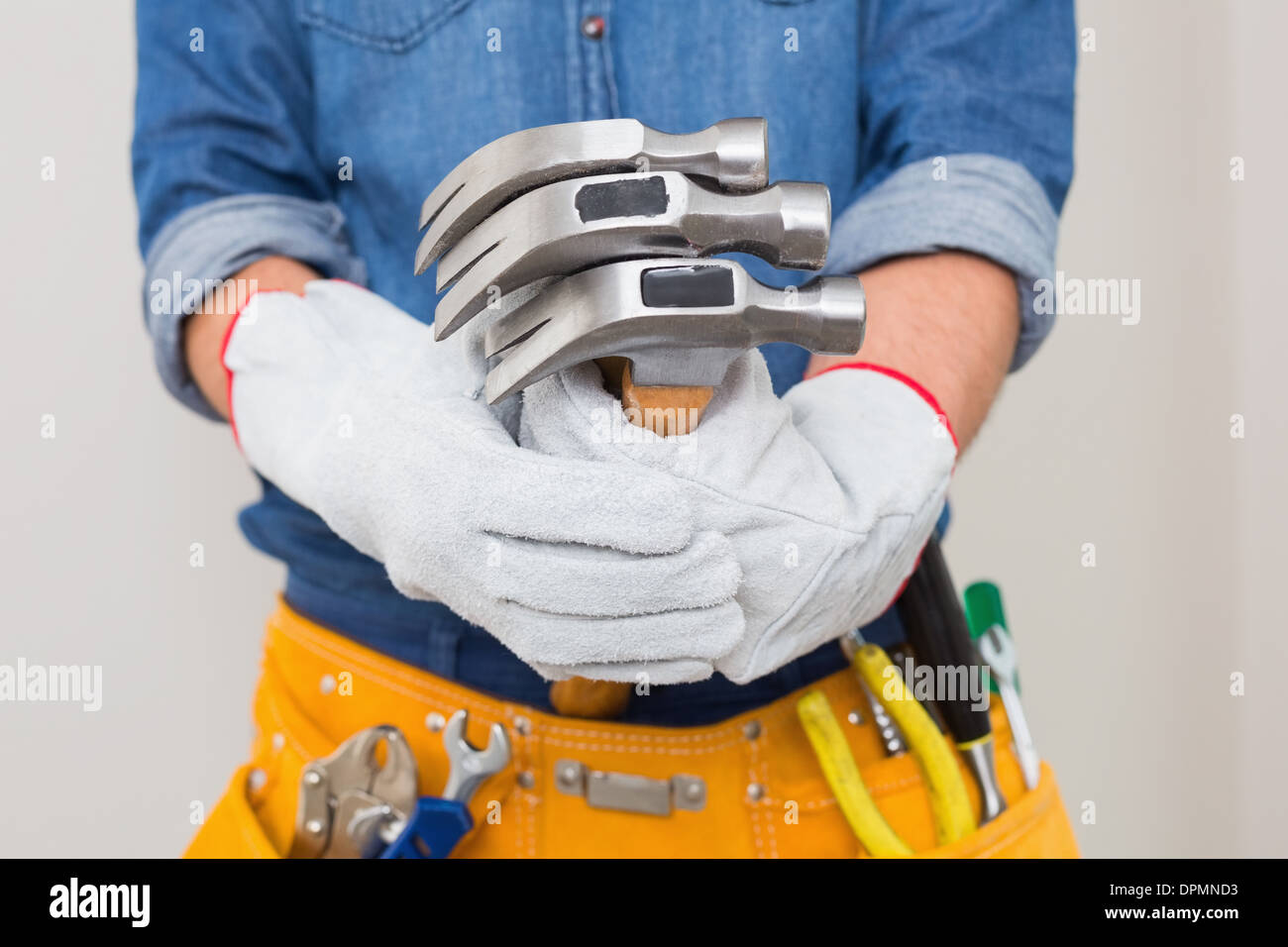 Mid section of handyman holding hammers with toolbelt around waist Stock Photo