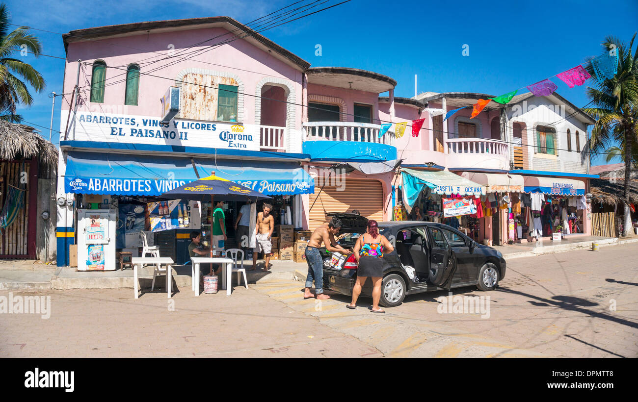 young vacationers load up their car with provisions outside grocery on colorful small scale main street of Zipolite beach town Stock Photo