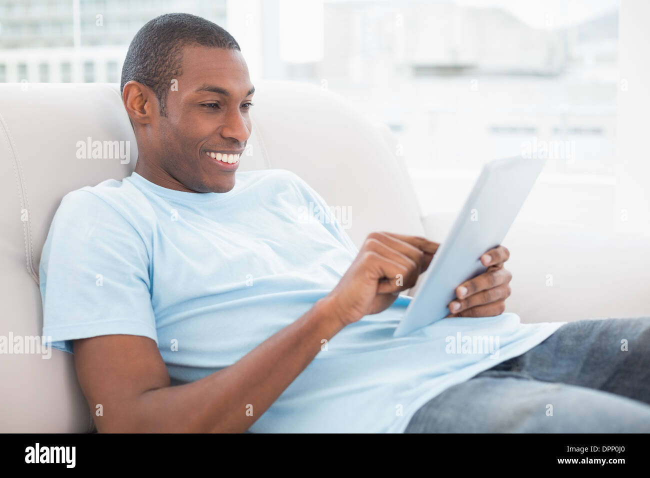 Casual smiling young Afro man using digital tablet on sofa Stock Photo