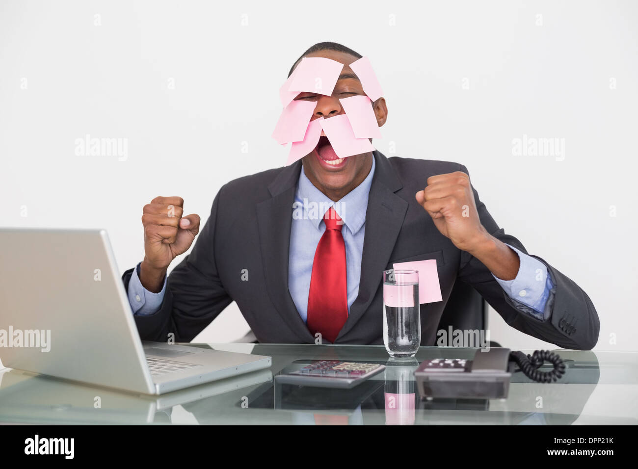 Frustrated Afro businessman with blank notes on face and laptop Stock Photo