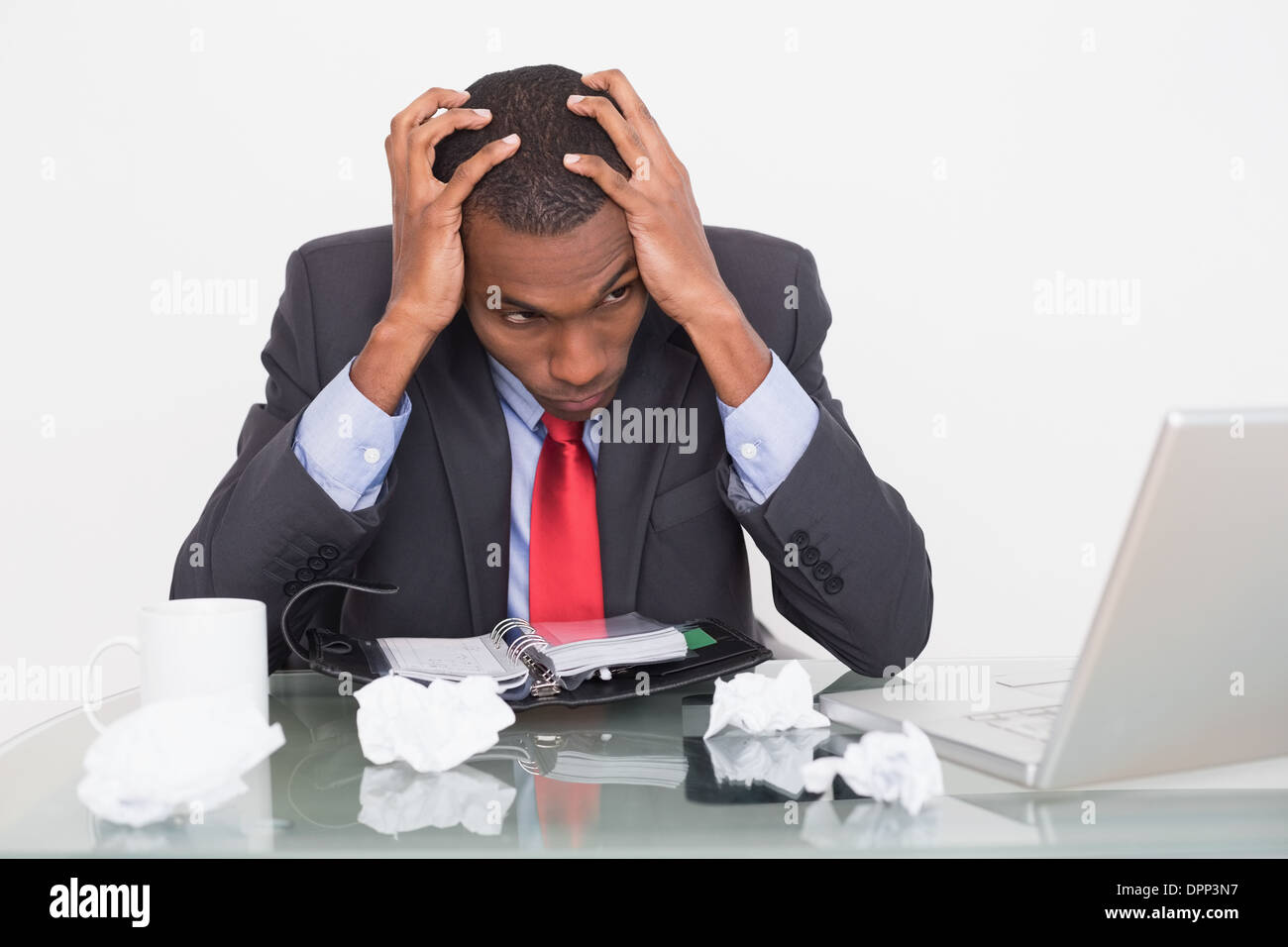 Frustrated Afro businessman with head in hands at desk Stock Photo
