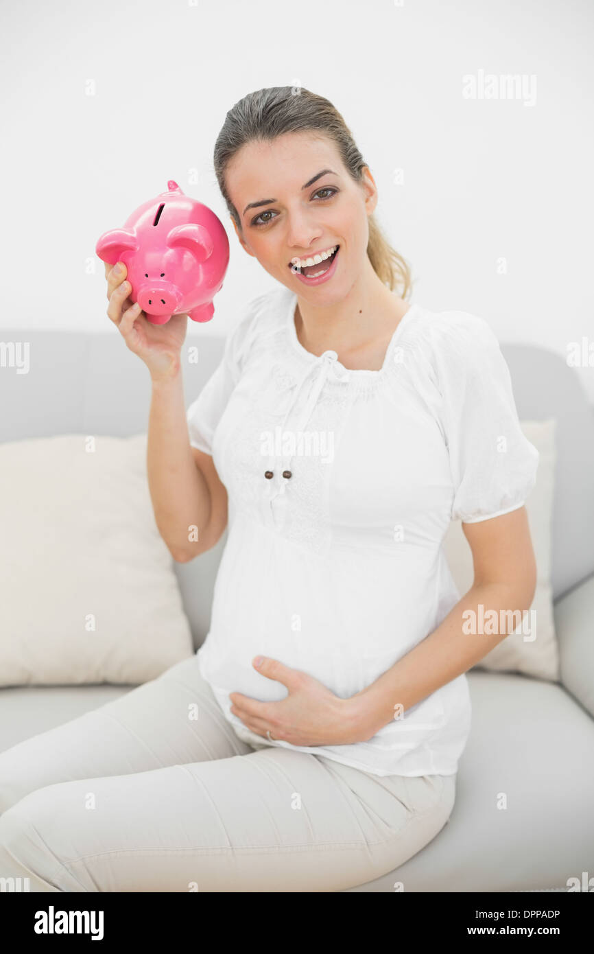 Beautiful pregnant woman shaking a piggy bank while holding her belly